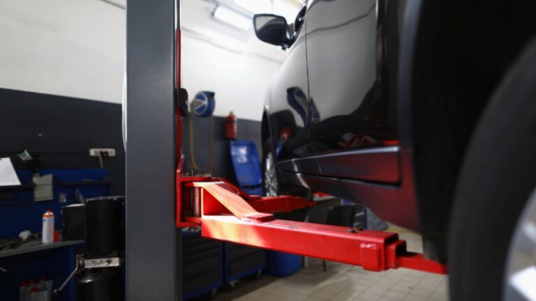 A dark SUV raised on a red hydraulic lift in a vehicle service bay